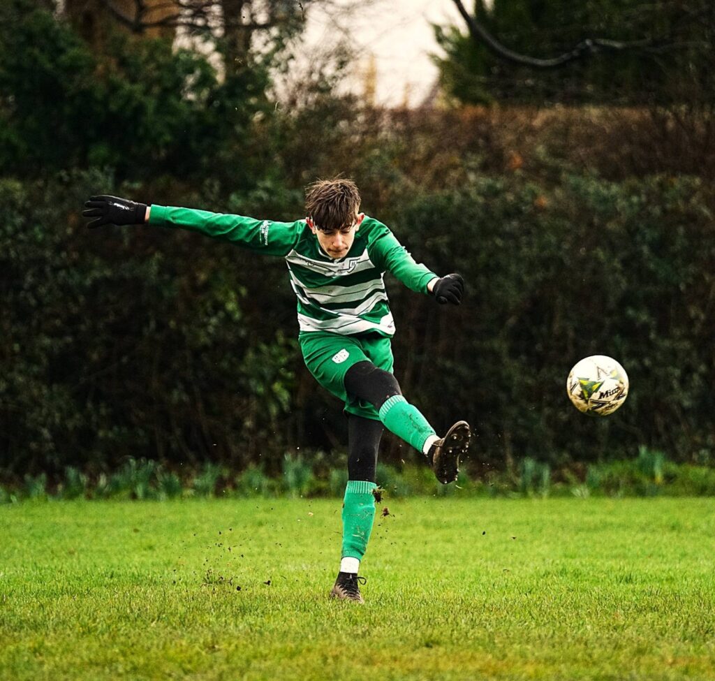 Holy Name FC football player striking a ball in a custom MG Sportswear Football Kit